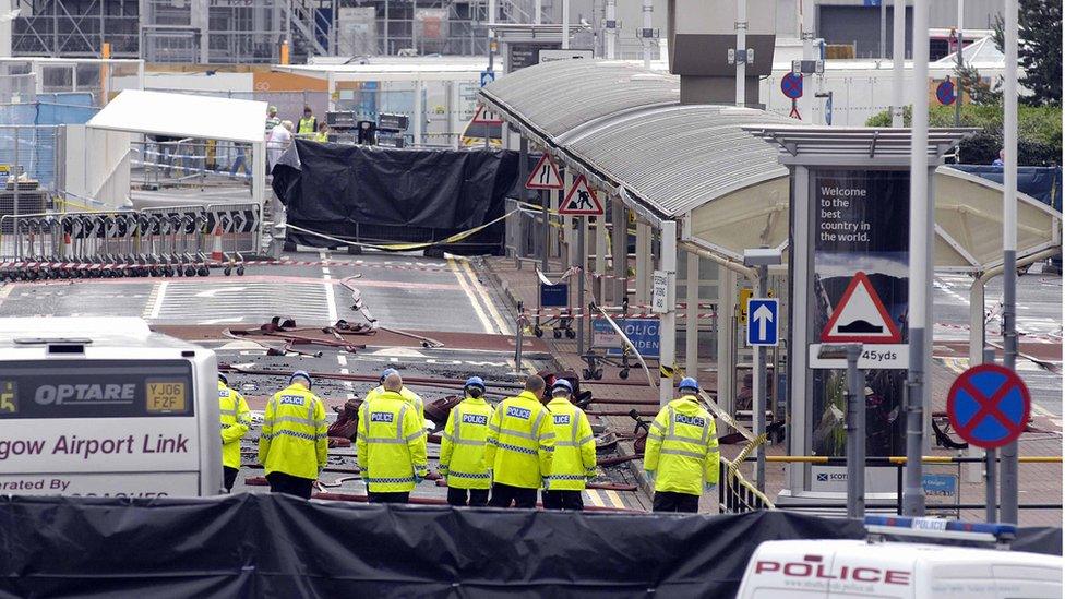 Police officers search the area where a burning car slammed into a terminal at Glasgow airport a day after the attack