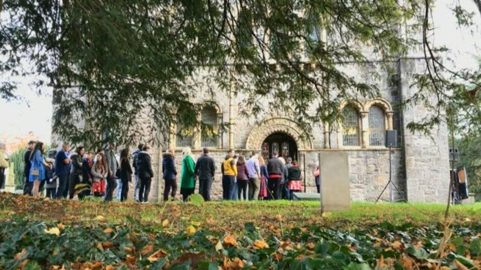 Mourners in bright clothes lining up outside a church