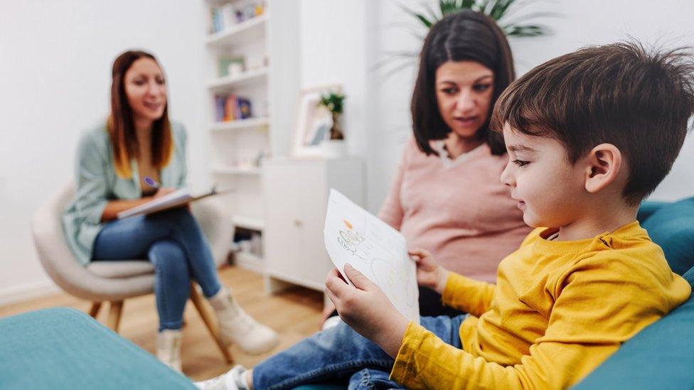 Child looks at picture with two adults nearby