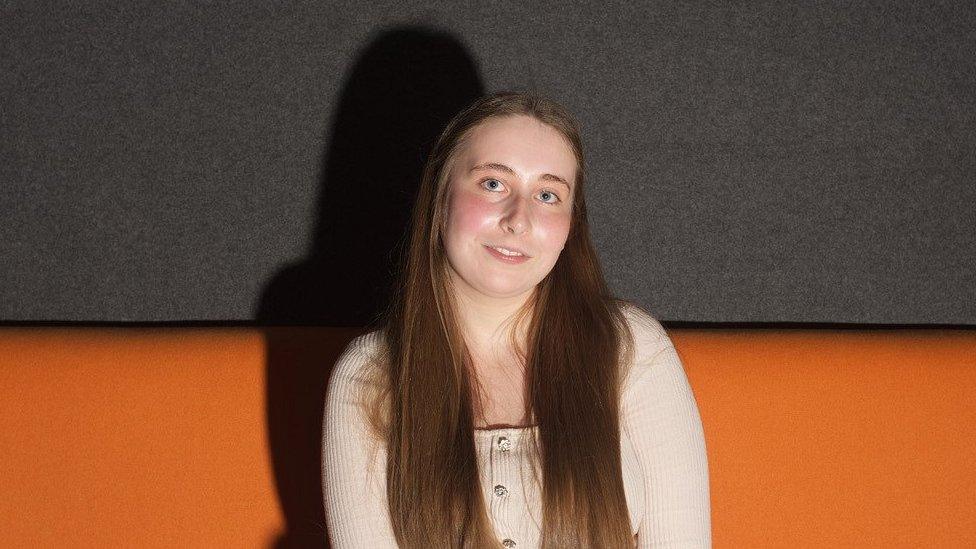 Gracie O'Grady, 18, sitting on an orange and black sofa at Harlow College