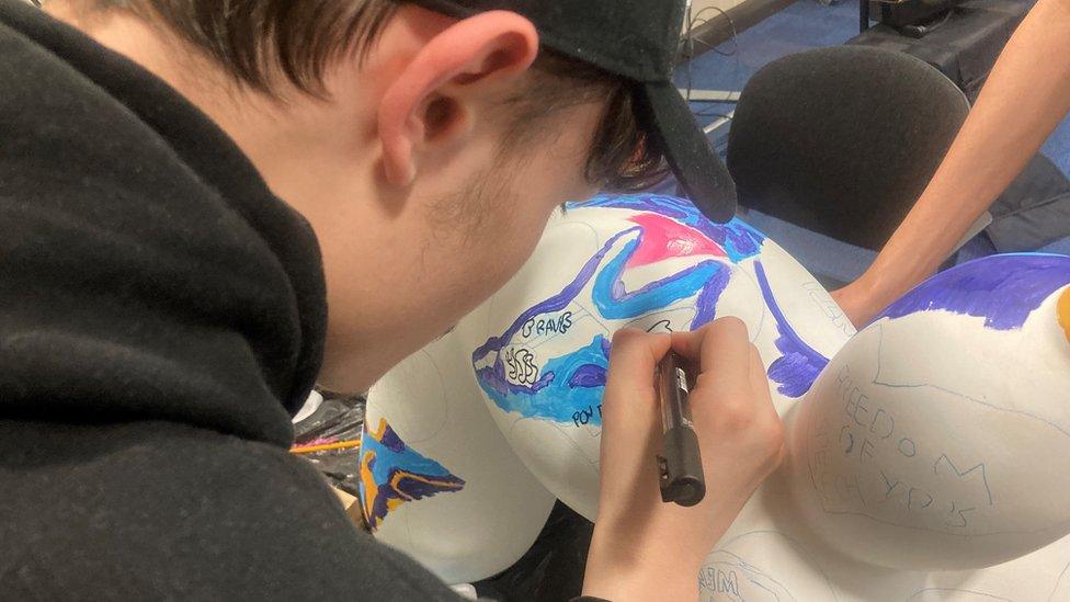 Teenager wearing a baseball cap painting the balloon dog sculpture with bright colours in the hope it will make people stop and consider the messages of equality painted onto the swinpup