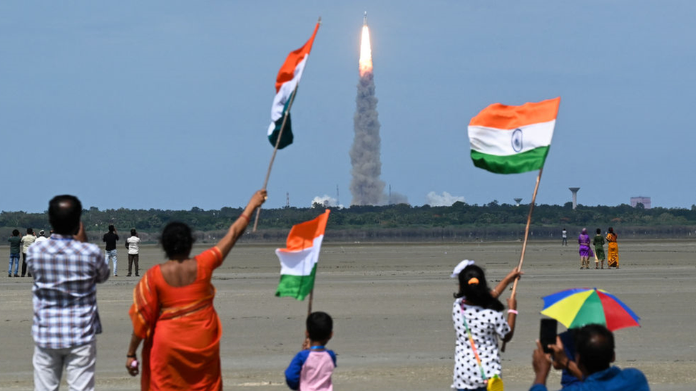 People wave Indian flags as an Indian Space Research Organisation (ISRO) rocket carrying the Chandrayaan-3 spacecraft lifts off in July