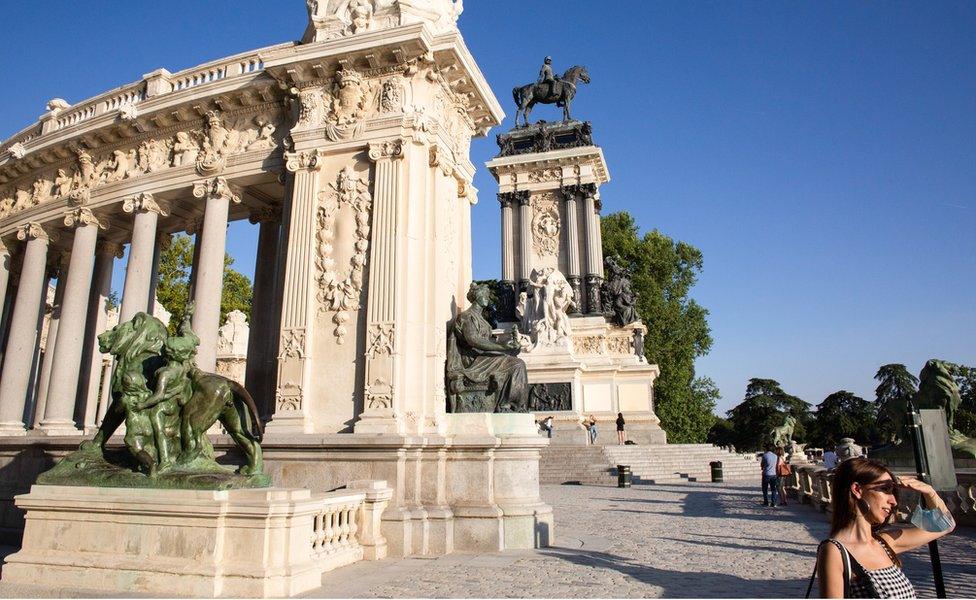 A woman covers her face from the sun and behind the Monument to Alfonso XII, which was built in 1922 in the Retiro park