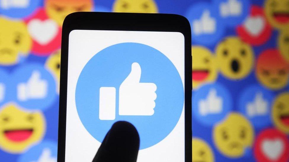 In this photo illustration a thumb up sign emoji and smiley face icons of Facebook are seen displayed on a mobile phone and a pc screen.