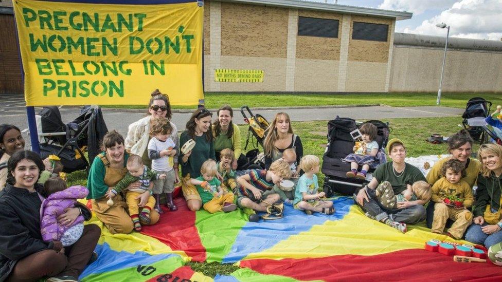 Protesters sit outside the prison on a colourful mat in a circle, holding banners