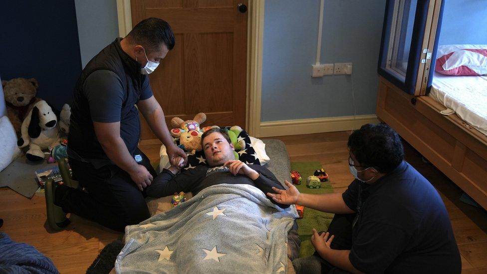 Oscar lying under a blanket as his carers interact with him.