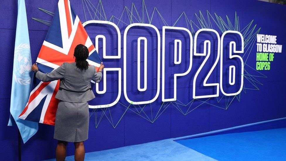 A summit organiser adjusts flags before the arrival of leaders for the COP26 UN Climate Summit in Glasgow on 1 November 2021