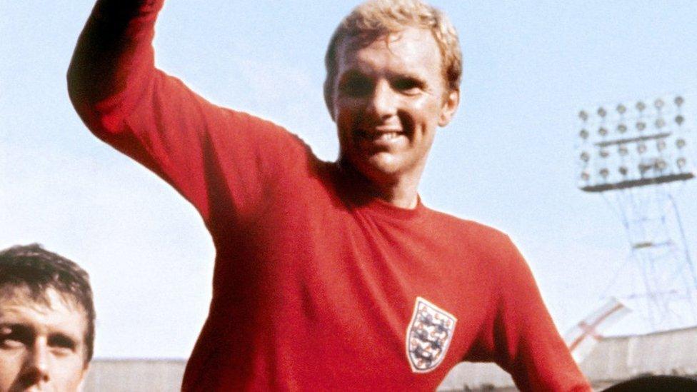 Sir Bobby Moore in the iconic red England shirt holding the World Cup trophy