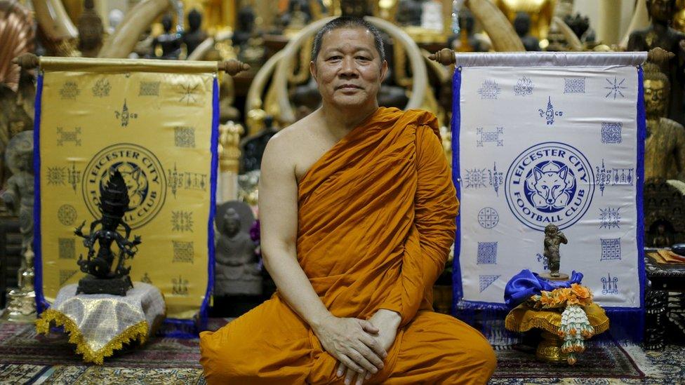 Thai Buddhist monk Phra Prommangkalachan holding a banner emblazoned with sacred patterns surrounding Leicester City Football Club's crest as he poses for pictures at the Traimitr Withayaram Woraviharn Temple in Bangkok