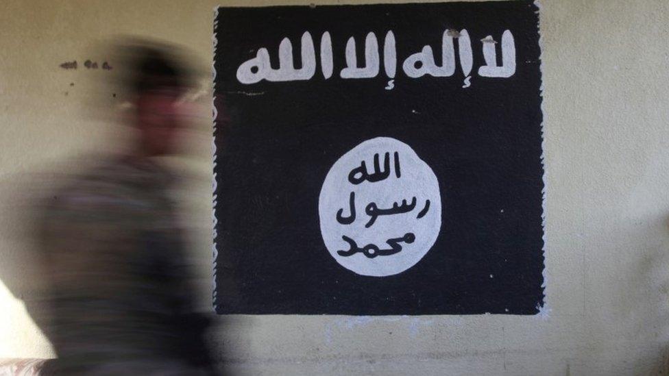 An Iraqi soldier walks past an IS flag in Mosul, file photo