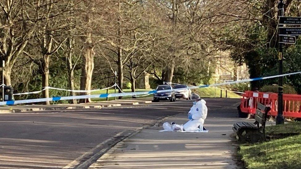 An investigator in white outfit kneeling on the floor behind police tape