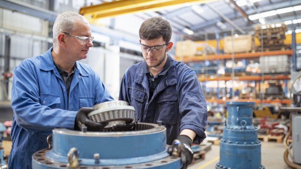 Older and younger worker inspect a giant cog