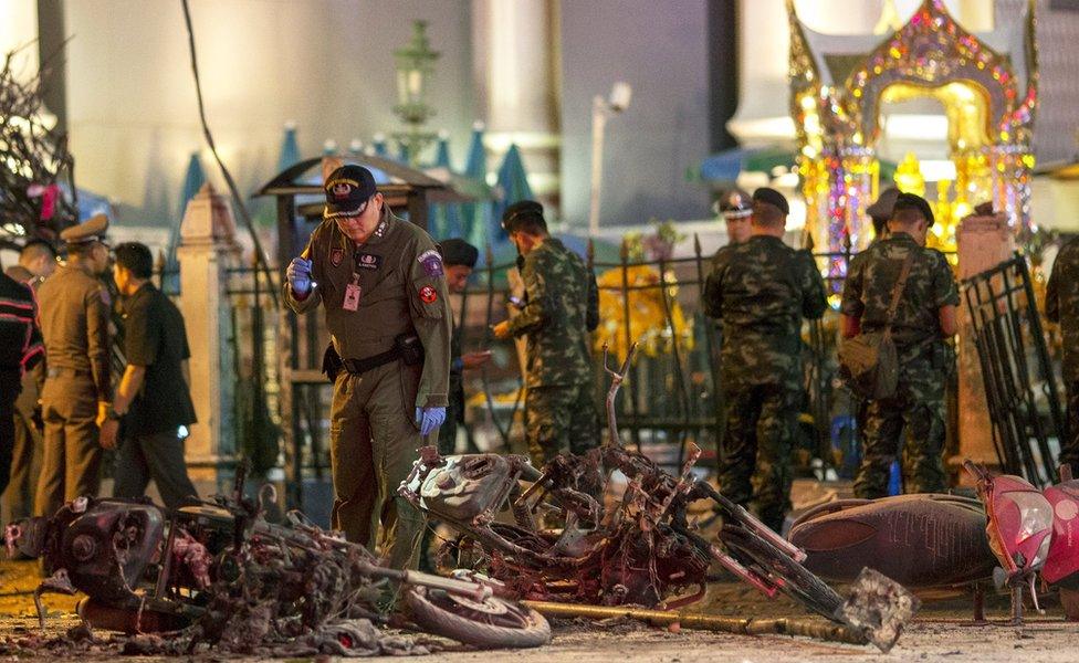 Experts investigate the devastated Erawan Shrine, 17 August 2015. A man in uniform looks at wrecked motorbikes, while others in uniform stand in the background.