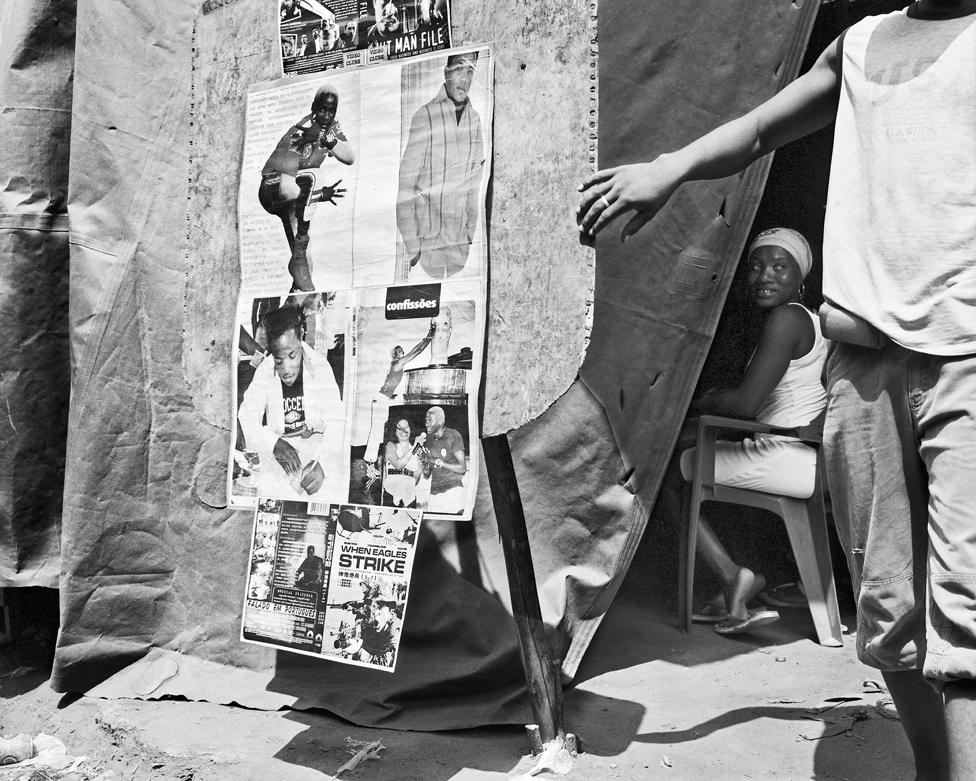 Black and white photo of a seated woman looking out from a tent decorated with posters