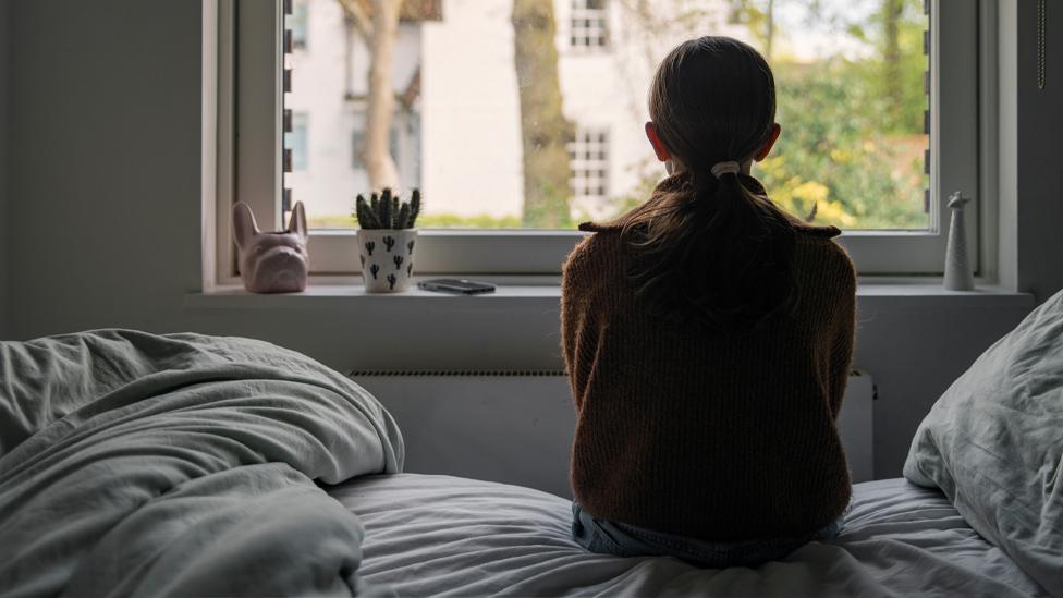 Anonymous girl looking out of a window, viewed from behind