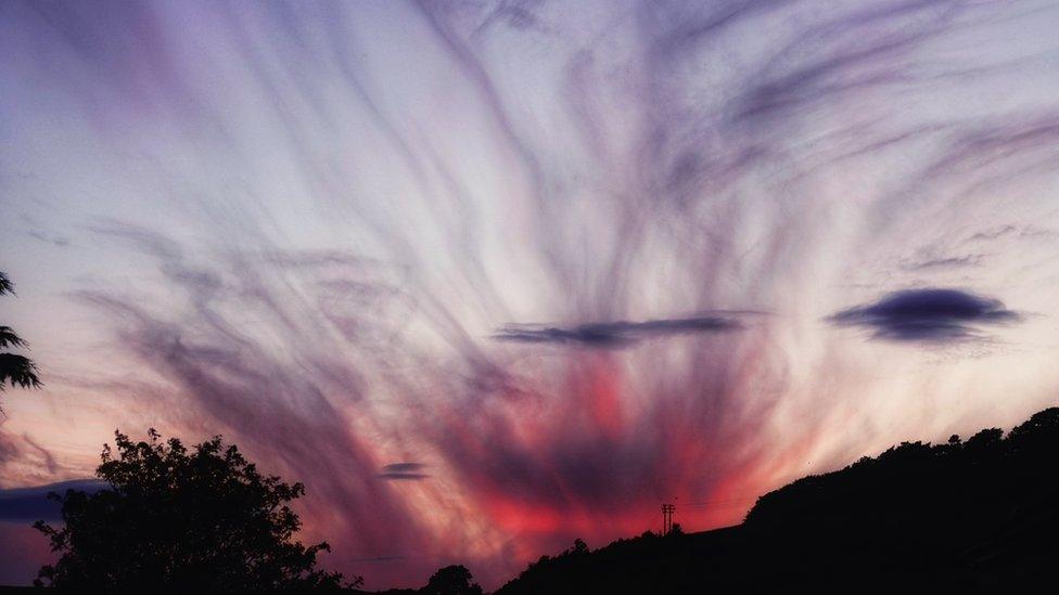 A vivid sunset of bright pinks, purple and blues with the silhouette of hills in the foreground