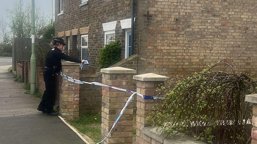 Police officer tying police tape around a brick gate pillar