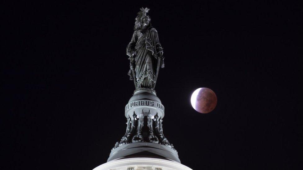 Partial lunar eclipse occurring behind "The Statue of Freedom", the bronze statue atop the US Capitol Building in Washington, DC, USA