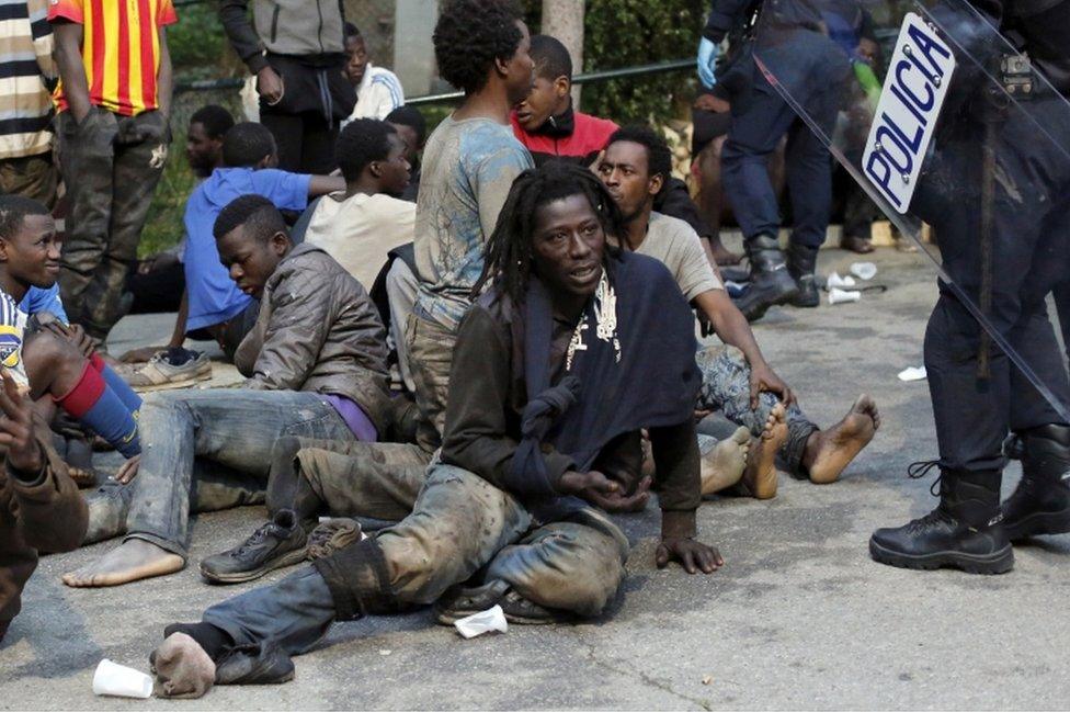 Migrants sit on the ground next to Spanish police officers after storming a fence to enter the Spanish enclave of Ceuta on 17 February 2017