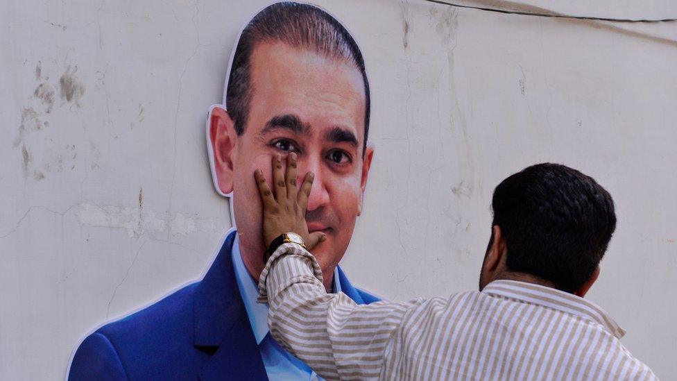 An Indian supporters of the Congress Party keeps his hand on the face of a cut out of billionaire jeweller Nirav Modi during a protest in New Delhi on February 16, 2018.