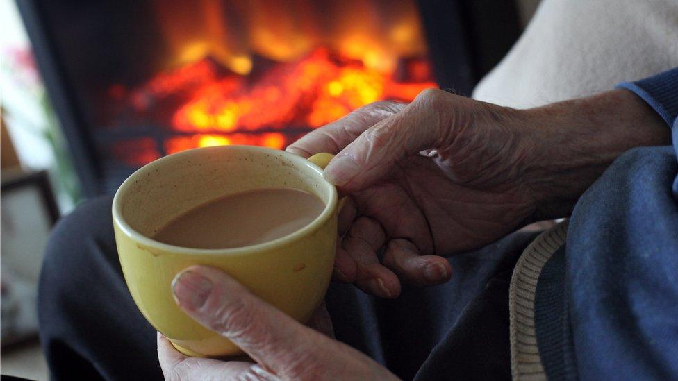 older person with cup of tea in front of fire