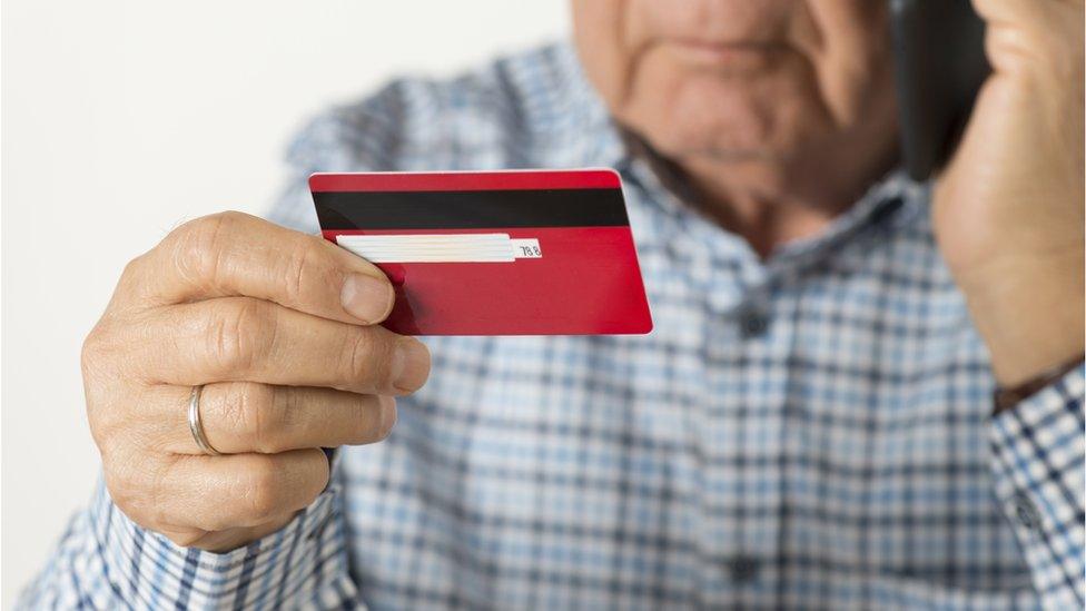 elderly man holding credit card while on the phone