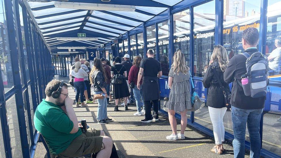 A long line of commuters waiting to board a bus.