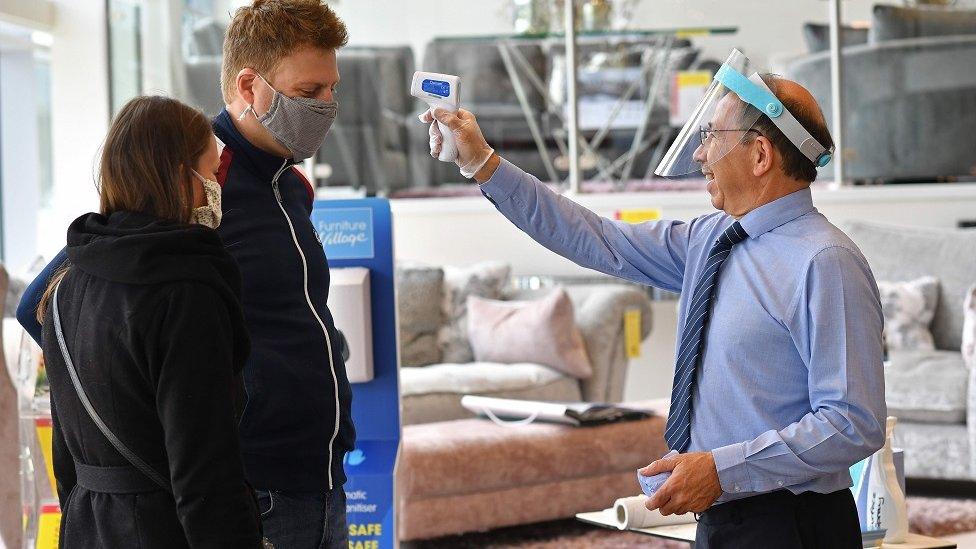 A member of staff wearing a face shield uses a laser thermometer to test a customer"s temperature in a Furniture Village store in Croydon, in south-east London on June 5, 2020, following the easing of the lockdown restrictions during the novel coronavirus COVID-19 pandemic.