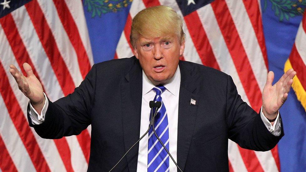 President Trump at a campaign rally in 2015, looking confused and angry and with US flags in the backround