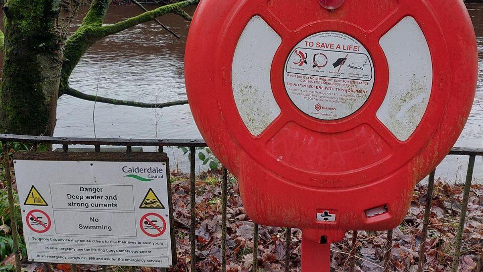 A lifebuoy and safety sign next to the River Calder