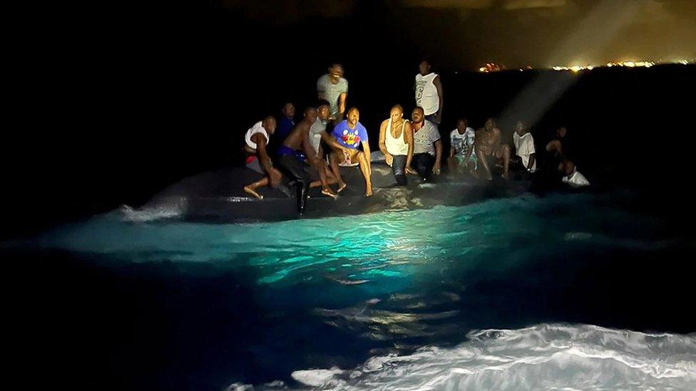 Survivors of a migrant boat that capsized perch on the overturned vessel off the coast of New Providence