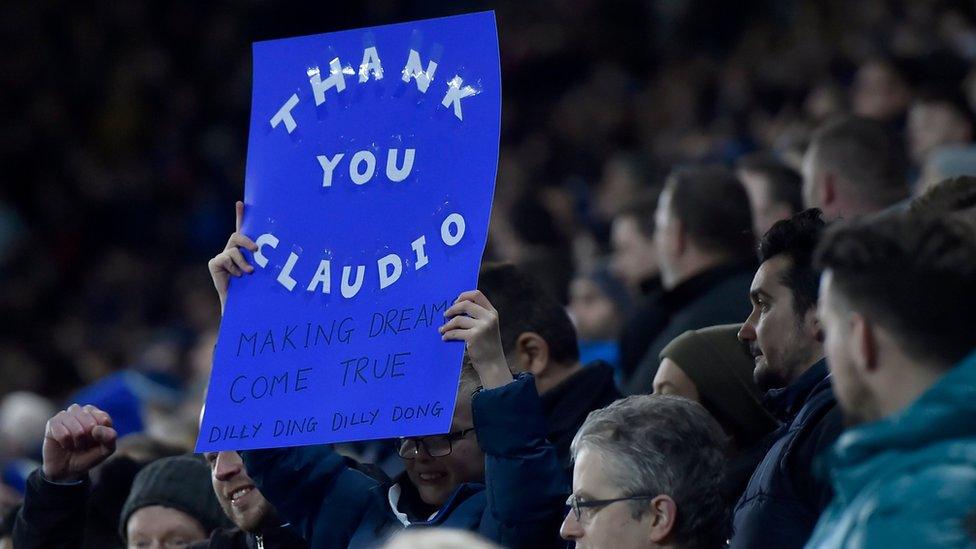 A fan holds up a sign during the English Premier League soccer match between Leicester and Liverpool at The King Power Stadium in Leicester,