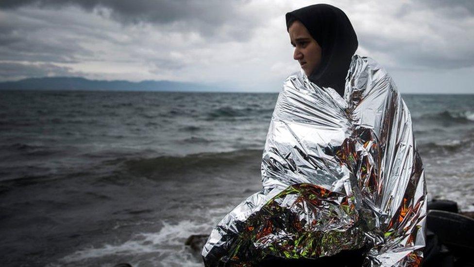 A woman tries to warm up herself using a thermal blanket provided by volunteers after arriving on a dinghy from a Turkish coast to the north-eastern Greek island of Lesbos, Saturday, Oct. 24, 2015