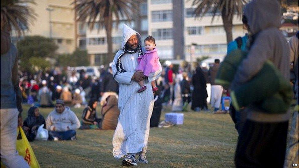 A man walks with a child as Muslim people congregate at Seapoint Promenade, a popular public area next to the sea, to try to sight the new moon, which will signify the end of the Muslim holy month of fasting, called Ramadan, on July 27, 2014.