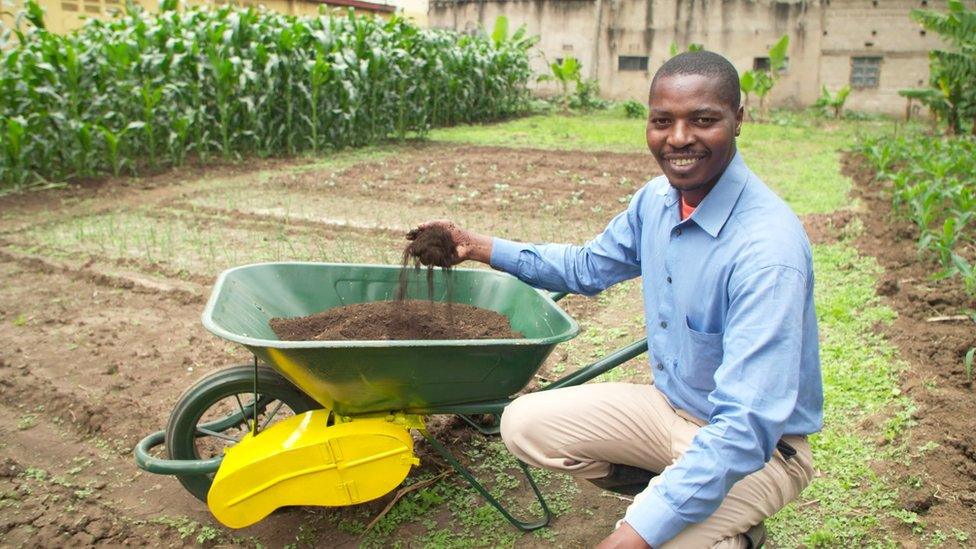 Frank Mollel kneeling by his "Fert Cart" invention