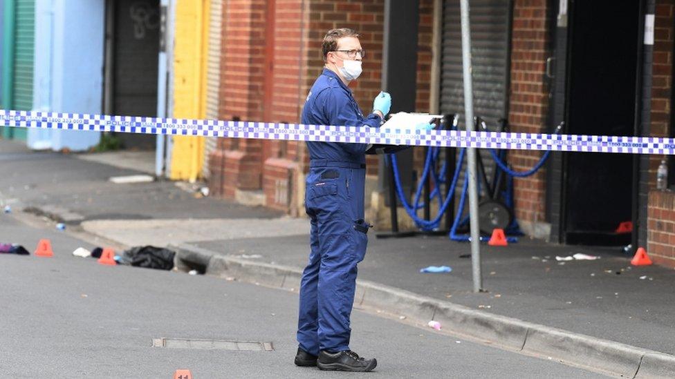 A forensic police officer is seen behind police line tape