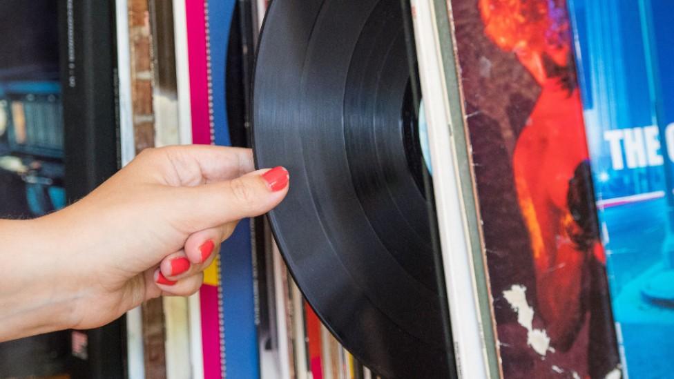 A hand removing a vinyl record from a shelf