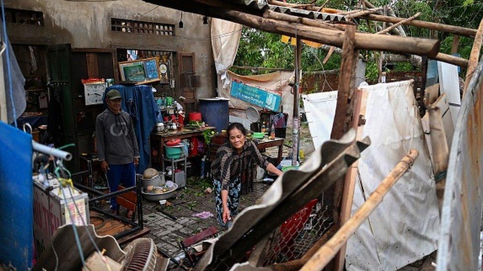 A woman clears debris from inside her house after it got damaged by the typhoon