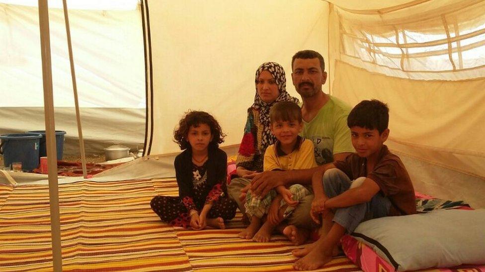 Two adults and three children sit inside a tent, May 2016