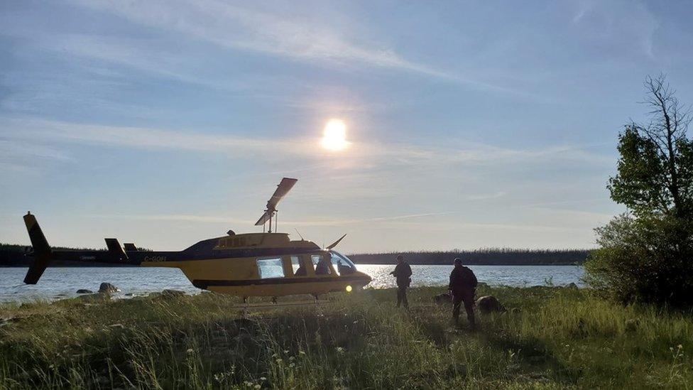 Police approach a search helicopter in the Manitoba wilderness.