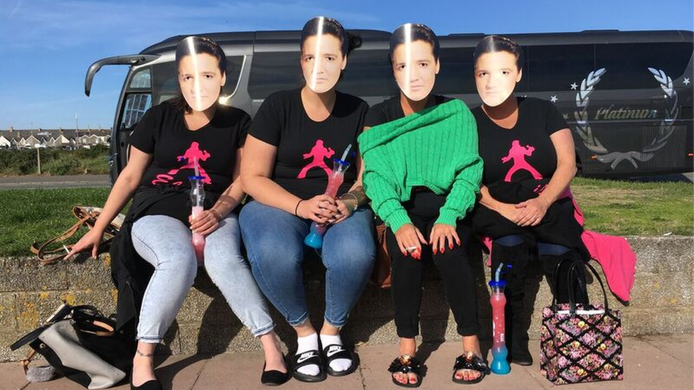 Four girls sat on a curb in Porthcawl with Elvis masks on