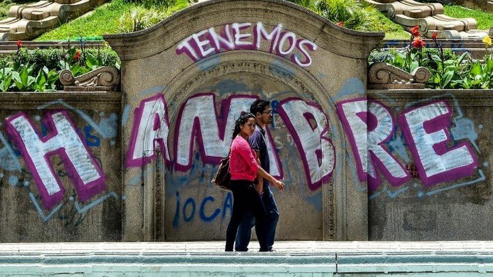 A couple walks by graffiti reading "We Are Hungry" in Caracas on August 8, 2017.