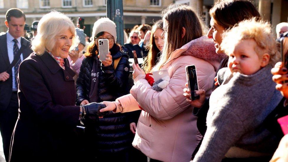 Queen Camilla, wearing a black coat, greeting people in Bath