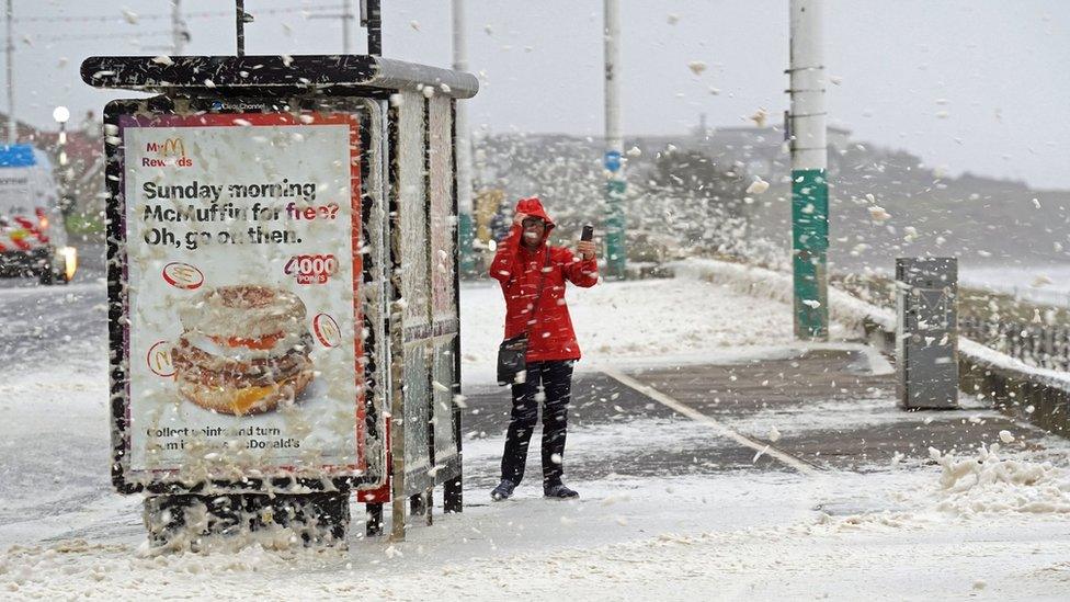 A member of the public in a flurry of sea foam caused by Storm Babet