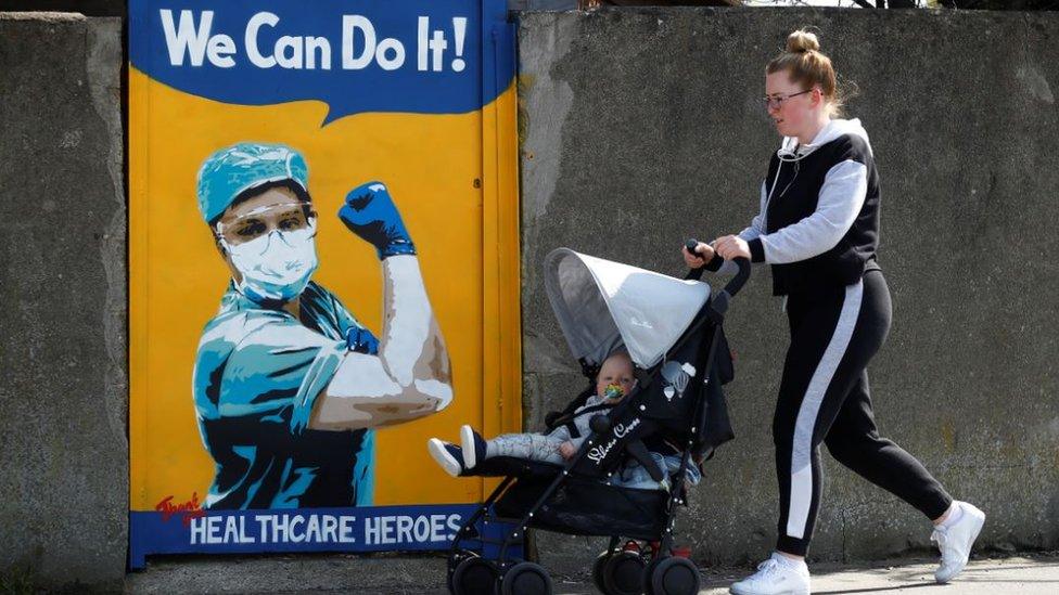 A woman pushes a child in a buggy past an NHS mural by Emma Blake in Dublin