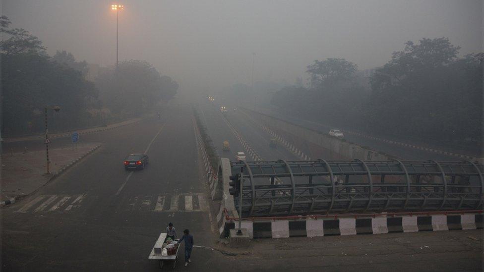 A street vendor pushes his cart on a road enveloped by smoke and smog, on the morning following Diwali festival in New Delhi, India, Monday, Oct. 31, 2016.