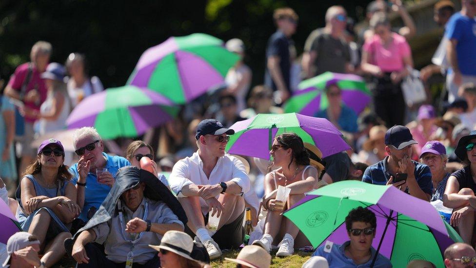 Spectators shield from the sun on day twelve of the 2022 Wimbledon Championships