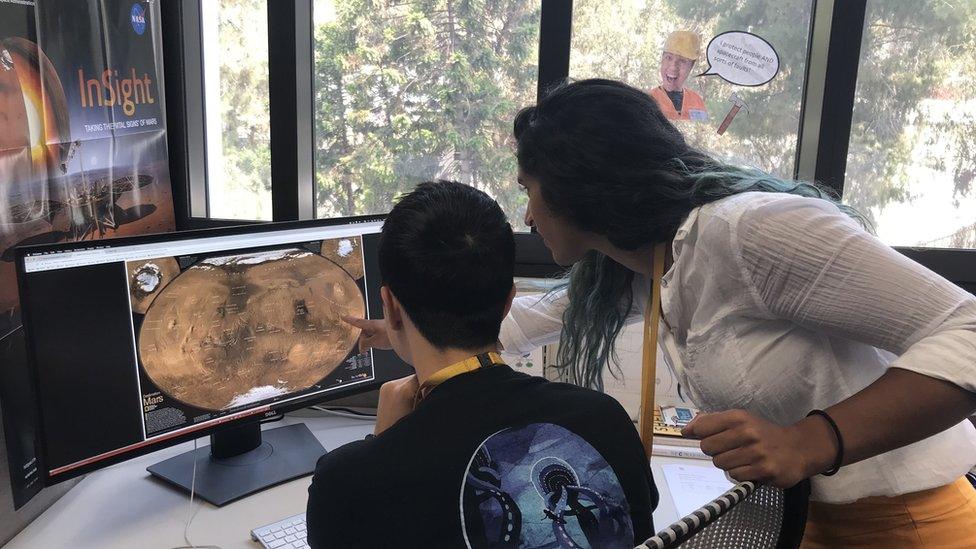 Two people look at a screen with a map of Mars - we are looking over their shoulders