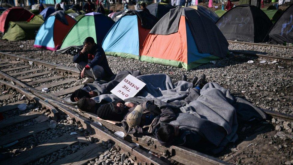 Men lay on railway tracks as a form of protest as they hold a banner reading "Open the border" at a makeshift camp by the Greek-Macedonian border near the village of Idomeni, 20 March 2016