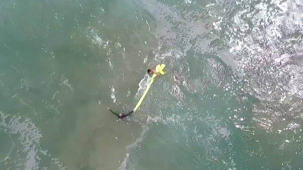 A screengrab shows the two boys clinging to the yellow inflatable as they swim back to shore